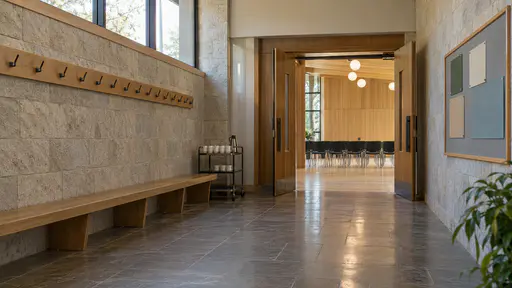 A long corridor outside a community hall has a continuous wooden bench along one wall with coat hooks above it, a tea trolley with stacked cups at one end and a double door ajar to the hall beyond in warm hall light.