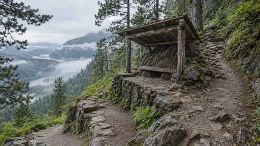 A hillside hiking switchback in cool morning light has a small landing at the bend under a little timber lean-to roof sheltering a flat stone resting ledge with the path clear on both sides climbing through pines and ferns and mist in the valley below.