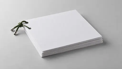 A green cord treasury tag with a stiff metal tip at each end passes through two punched holes at the top-left corner of a neat stack of about ten blank white sheets lying flat on a plain pale grey surface.