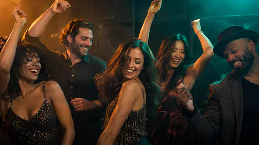 Five fictional adults in evening clothes dance close together with raised arms on a club dance floor in a cinematic photograph lit by warm amber and cool teal gels.