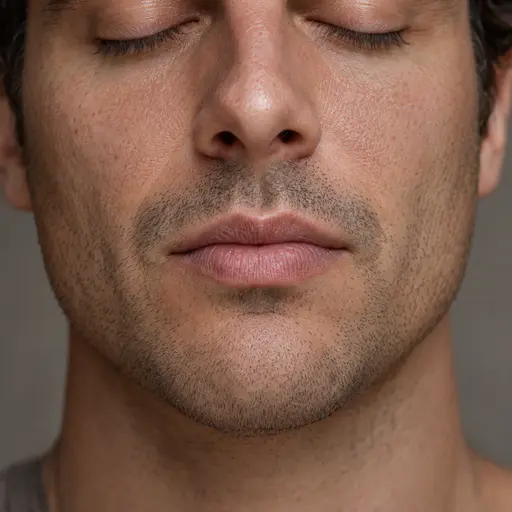 A fictional adult man photographed from nose to chin has relaxed closed lips and a soft stubble shadow under an elevated frontal key against a plain warm grey backdrop.