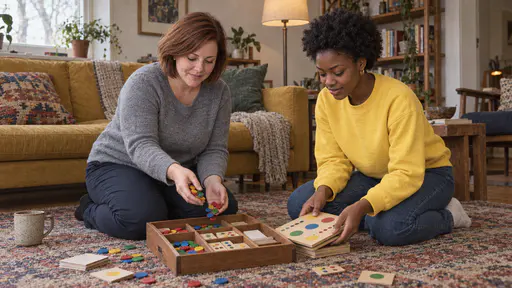 A woman with a chin-length auburn bob in a grey sweater and a young woman with a natural afro in a yellow sweatshirt kneel on a rug sorting coloured counters into the compartments of a wooden game box beside a folded board in soft late light.