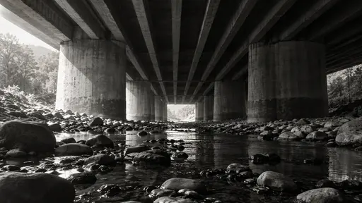 The underside of a concrete road bridge with massive piers and repeating ribbed beams seen from a dry riverbed with a thin stream and round stones.