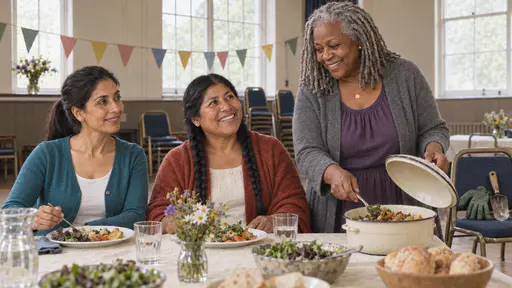 A woman with a ponytail in a teal cardigan and a woman with two braids in a terracotta shawl sit side by side at a long table while a woman with silver locs in a purple dress serves them from a covered dish in soft window light.