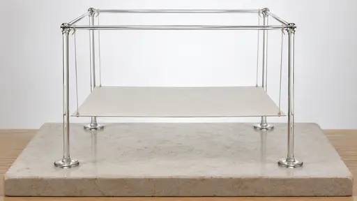 A frame of four upright and four horizontal thin clear glass rods on a pale stone plinth suspends a flat white paper platform by four thin paper strings from its top corners, the platform hanging level below the frame.