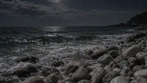 Low surf meets a bank of round pale pebbles at the top of a night beach with the water sliding back between the stones in dim light.