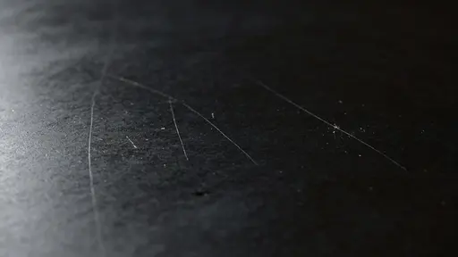 Close-up product-style study of a matte black surface with fine scratches, photographed for background or wallpaper use with moody minimalist lighting and texture focus.