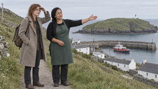 A Samoan woman with a long black braid in a green apron gestures with an open palm toward a distant headland with a small white lighthouse while a freckled woman with an auburn braid and a rucksack listens on a grassy island path above the harbour.