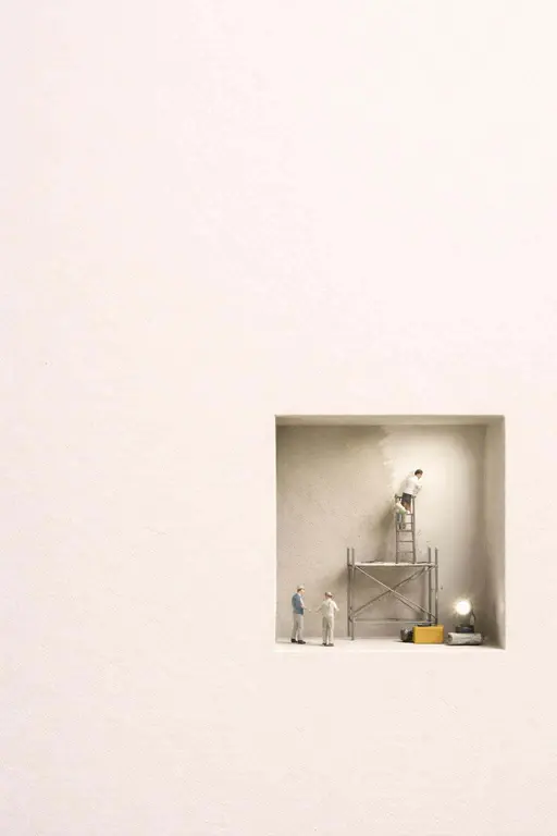 Portrait 2:3 scene of a minimal warm off-white paper surface with a small recessed cutout in the lower third revealing a miniature worksite with tiny workers, scaffold, and neat tools.
