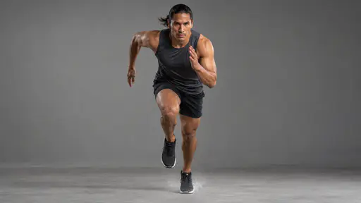 A fictional adult Native American athlete in a charcoal running top and shorts is frozen mid stride in a sprint toward the camera with chalk dust and flying drops of sweat in a studio.