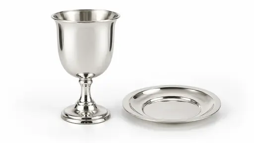 A plain silver kiddush cup on a short stem with a smooth bowl stands beside a small matching plate on a seamless white sweep with no engraving.