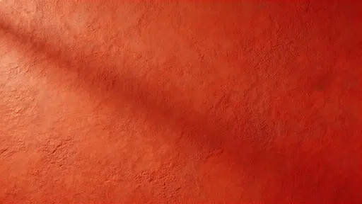 Widescreen 16:9 studio-style photograph of a minimal red plaster wall with subtle micro-variation and shallow relief, softly side-lit to reveal calm negative space.