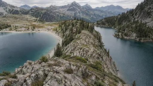 A rocky promontory divides a mountain lake into two sheltered bays with different shorelines visible beyond each in bright mountain light.