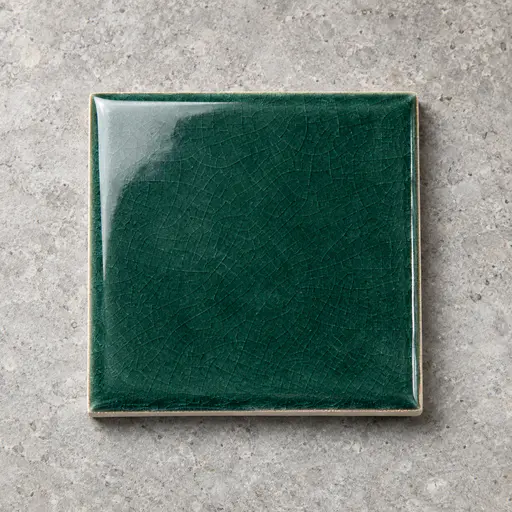 A single square sea green glazed ceramic tile with fine crackle and a chamfered edge showing pale biscuit clay lies on a pale grey stone slab.