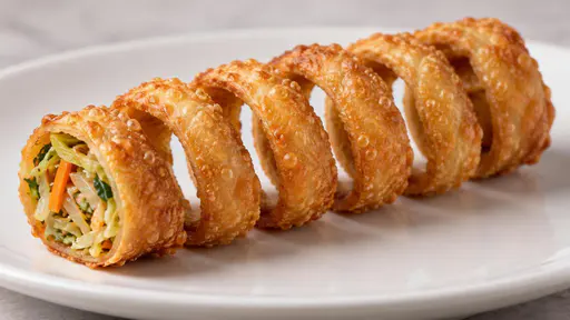 A golden fried spring roll sliced into a continuous open coil revealing shredded vegetable filling, on a white plate against a marble surface.