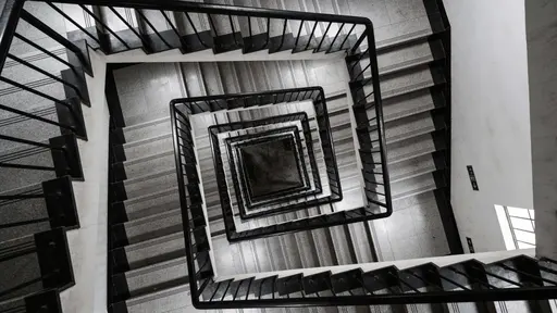 An intense architectural maze of tightly spaced staircases and narrowed corridors, concrete walls and metal railings creating repeating angular patterns and claustrophobic depth across a 16:9 horizontal frame.