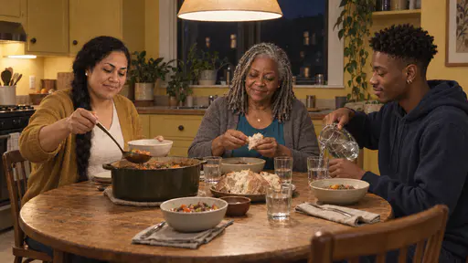 Three housemates share a supper at a round oak kitchen table under a hanging lamp, one ladling stew into bowls, one tearing bread and one pouring water, with a dark tall window behind them.