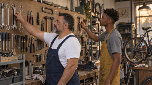 A stocky mechanic with a short grey beard in dark blue overalls hangs a large spanner on its painted outline while a tall young man in a mustard apron hangs a small hammer on its outline beside him on a pegboard tool wall in amber evening light.