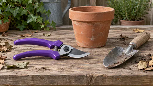 A pair of garden secateurs with violet plastic handles rests on a weathered potting bench beside a clay pot and a small trowel with a few dry leaf scraps on the boards in plain even light.