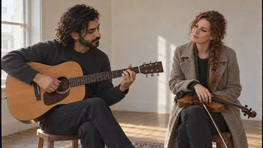 A freckled woman with a loose auburn braid sits with her violin lowered on her knee, head tilted, listening as a slim bearded man repeats a phrase on his acoustic guitar in a small rehearsal room in low side light.