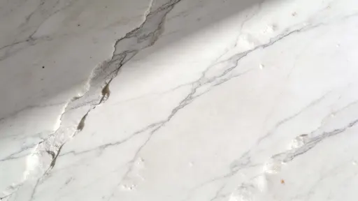 Top-down 16:9 photograph of a white marble surface with subtle gray veins, soft directional light, and minimal composition designed for clean wallpaper backgrounds.