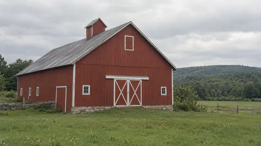 A whole red barn stands beside an open green field with its roofline complete against the sky in even daylight.