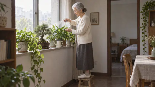 A very small elderly woman with silver-white hair in a low bun and jade earrings in a cream cardigan stands on a low stool misting a row of green houseplants and a small bonsai pine with a spray bottle on a sunny window shelf with a small watering can on the sill in soft morning light.