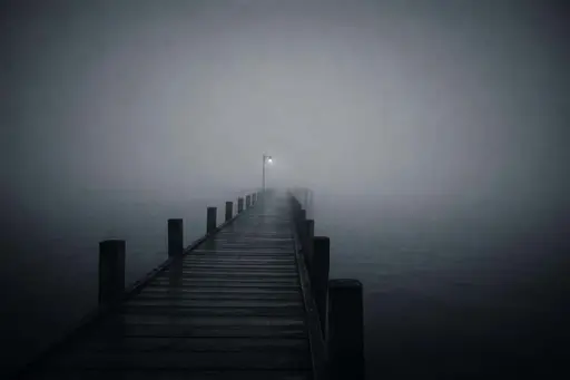 Minimal 3:2 widescreen cinematic photo of an off-center empty wooden pier stretching into dense cool fog over still water, evoking quiet sadness.