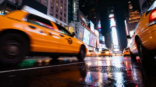 Long-exposure night view of yellow taxis streaking through Times Square with vivid neon reflections on realistic wet pavement and cinematic motion blur in 16:9.
